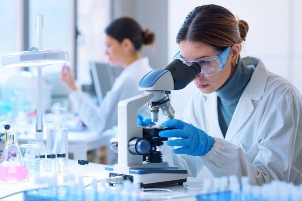 Young scientists conducting research investigations in a medical laboratory, a researcher in the foreground is using a microscope